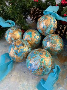 blue and gold ornaments are sitting next to pine cones on a table with ribbons around them