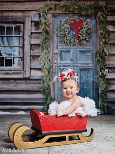 a baby sitting on a sled in front of a wooden building with wreaths