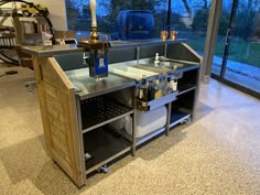 a kitchen island made out of wood and metal with bottles on the top, in front of a large window