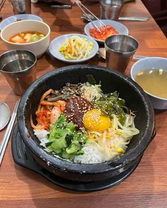 a bowl filled with rice and vegetables on top of a wooden table next to bowls of soup