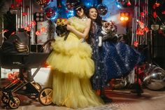 two women in dresses standing next to each other near a baby stroller and balloons