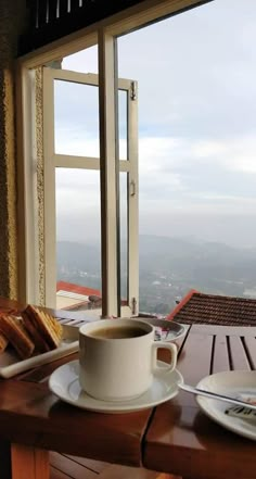 a cup of coffee and some bread on a table with a view out the window