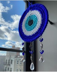 a blue and white crocheted dream catcher hanging from a window sill with the sky in the background