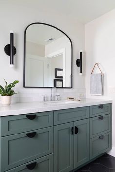 a bathroom with green cabinets and a large mirror on the wall above it, along with a potted plant