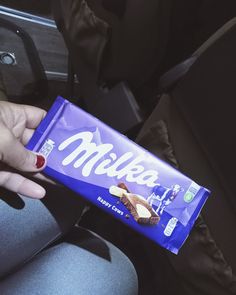 a person is holding a milk bar in their hand while sitting on a car seat