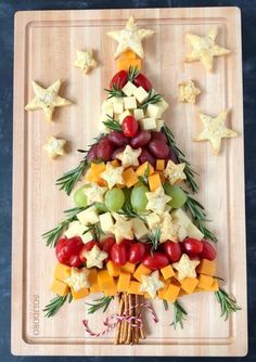 a christmas tree made out of cheese and fruit on a cutting board with stars around it