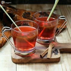 two glasses of tea with cinnamon sticks in them on a wooden tray next to a bag