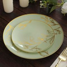 two green plates sitting on top of a wooden table next to candles and white flowers