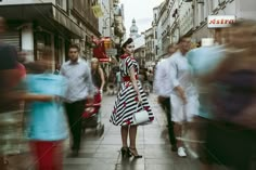 a woman in a striped dress is walking down the street while people walk by onlookers