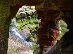 a waterfall is seen through an opening in a rock formation with moss growing on the rocks