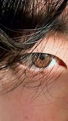 a close up of a person's eye with hair blowing in the wind