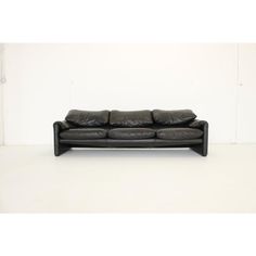 a black leather couch sitting on top of a white floor in front of a wall