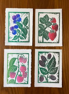 four small prints with flowers and berries in them on a wooden surface, one is green and the other is red