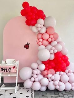 there is a pink and red balloon arch with ladybug balloons on the wall