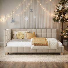 a white bed sitting next to a christmas tree in a room with lights on the wall