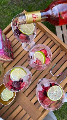 four glasses filled with fruit and wine on top of a wooden table next to a bottle