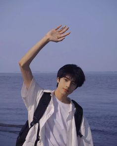 a man standing on top of a beach next to the ocean holding his hand up