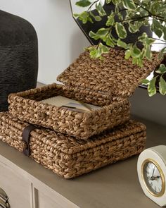 two wicker baskets stacked on top of each other next to a clock and plant