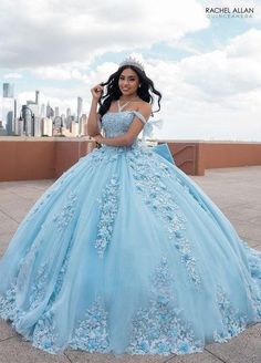 a woman in a blue dress standing on a roof with her hands behind her head