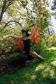 a woman sitting on top of a bench in the grass holding an orange shawl