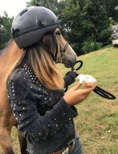 a woman wearing a helmet and holding a donut in front of a brown horse