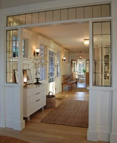 an open door leading to a living room and dining room with wood floors, white walls and windows