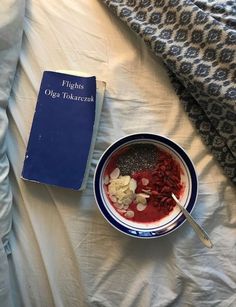 a bowl of cereal next to a book on a bed