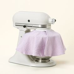 a white mixer with a purple towel on it's top and the bowl cover is folded up