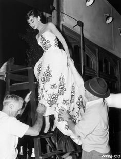 an old photo of a woman in a dress on a ladder being lifted by two men