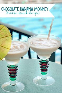 two glasses filled with white chocolate banana money drink next to an umbrella and swimming pool