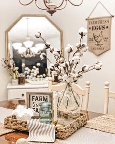 a wooden table topped with a glass vase filled with flowers and cotton floss next to a mirror