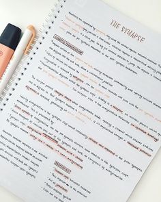 two pens sitting on top of a notebook next to an orange and white marker pen