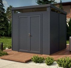 a large gray shed sitting on top of a wooden deck next to a tree and bushes