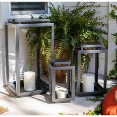 three metal lanterns sitting on top of a porch next to a potted plant and an orange pumpkin