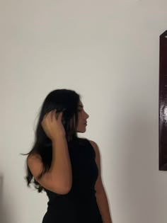 a woman in a black dress talking on her cell phone while standing next to a mirror