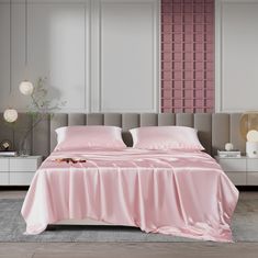 a bed with pink sheets and pillows in a white room next to a gray headboard