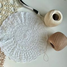 crocheted doily, yarn and scissors on a white tablecloth with two balls of thread