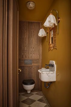 a bathroom with a toilet, sink and wooden paneled walls in the background is a checkered floor