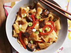 a white bowl filled with pasta and vegetables next to chopsticks on a table