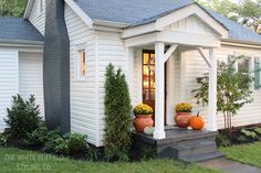 a small white house with two pumpkins on the front porch and an entry way