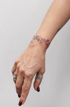 a woman's hand with two rings on it and a flower tattoo on the wrist