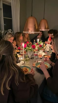 a group of people sitting around a table with plates of food and candles in front of them