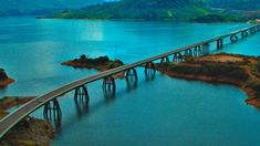 an aerial view of a bridge spanning the width of a body of water with mountains in the background