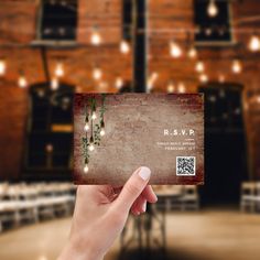 a person holding up a business card in front of a brick wall with lights on it