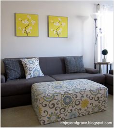 a living room with two paintings on the wall and a ottoman in front of it