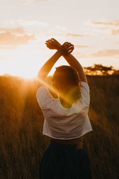 a woman standing in the middle of a field with her hands up to her head