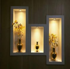 three vases with yellow flowers in them are lit up by lights on the wall