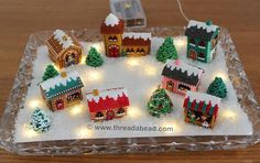 a glass tray with christmas decorations on top of it and lights around the houses in the snow