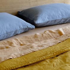 two pillows on top of a bed with yellow sheets and blue pillow cases next to each other