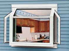 an open window in the side of a blue house shows a kitchen with wooden cabinets and white appliances